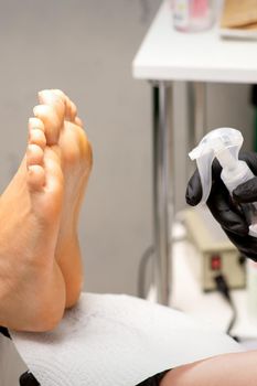 Pedicure master disinfects the feet of woman with the preparation decontamination in beauty salon
