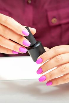White woman holding nail polish black bottle with painted pink nails close up