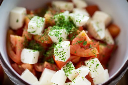 salad of fresh ripe tomatoes with mozzarella and spices in a bowl on a wooden table