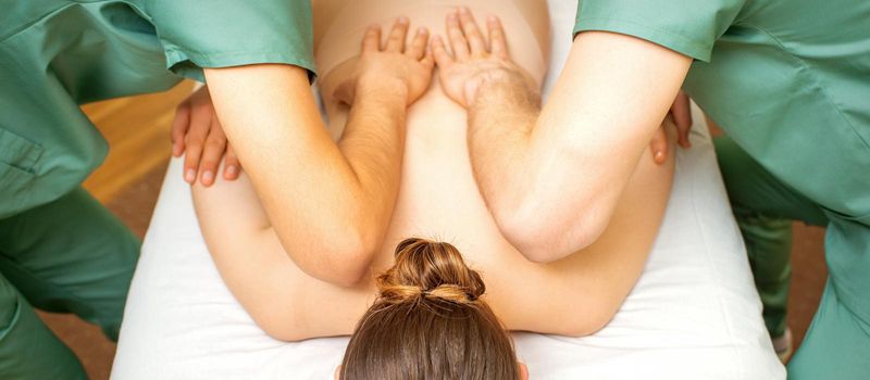 Back and hands double massage with four hands of two professional massagers for a young caucasian woman in a spa salon