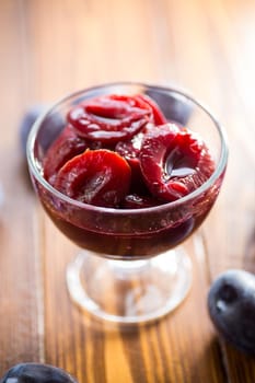 Sweet plums in syrup, in a glass bowl on a wooden table.
