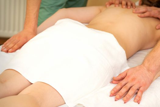 Back and hands double massage with four hands of two professional massagers for a young caucasian woman in a spa salon