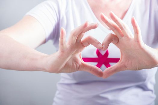 woman making heart sign with fingers on breast cancer protection symbol background. High quality photo