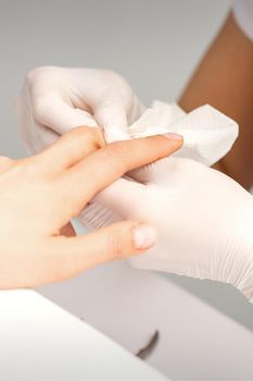 Manicure master wiping the moisturizer from the end of female fingers in beauty salon