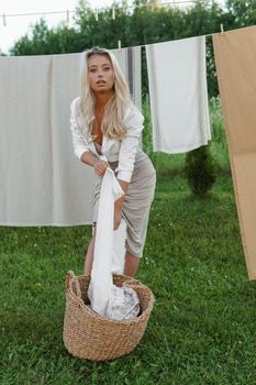 Laundry day. A woman hangs linen and towels on a tree in the courtyard of a village house. Summer cottage concept.