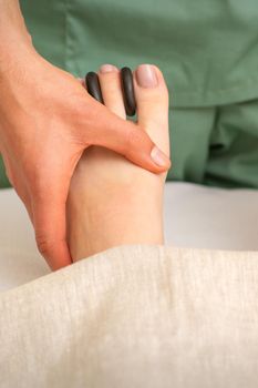 Massager doing feet and toes massage with rocks between a female toes