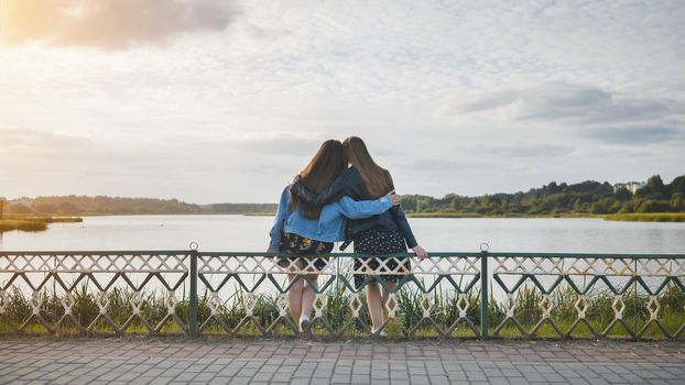 Two girlfriends sitting in an embrace on the lake shore