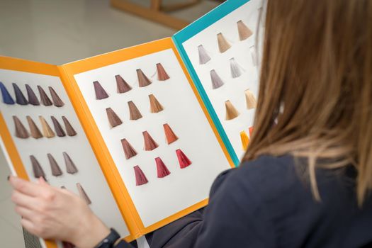 Young brunette woman choosing hair color from palette samples at the beauty salon, hair dyeing concept