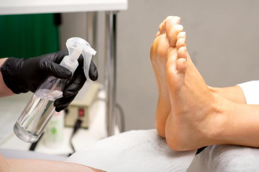 Pedicure master disinfects the feet of woman with the preparation decontamination in beauty salon