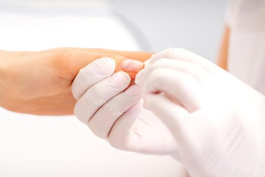 Manicure master wiping the moisturizer from the end of female fingers in beauty salon