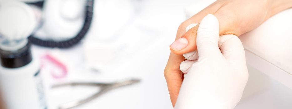 The manicurist holds the female thumb during a manicure procedure in the nail salon