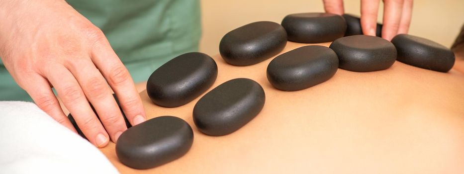 Young caucasian woman receiving back massage with black stones by masseur in spa salon. A woman getting a spa treatment