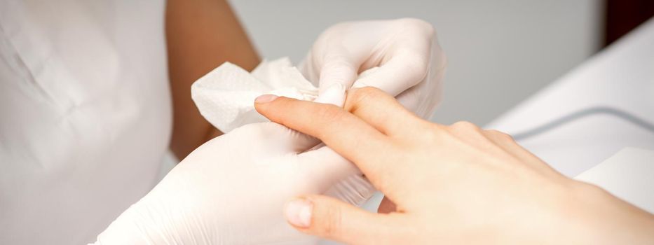 Manicure master wiping the moisturizer from the end of female fingers in beauty salon