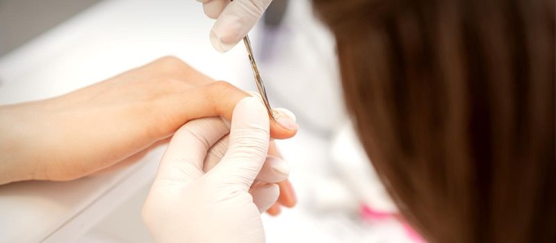 Close up of manicure master with manicure scissors removes cuticles on female nails at a beauty salon