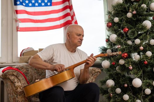 Man playing acoustic guitar, American flag, at christmas.