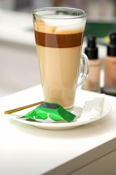 A cup of latte with candy on a saucer on the table in the manicure room. Manicure master place