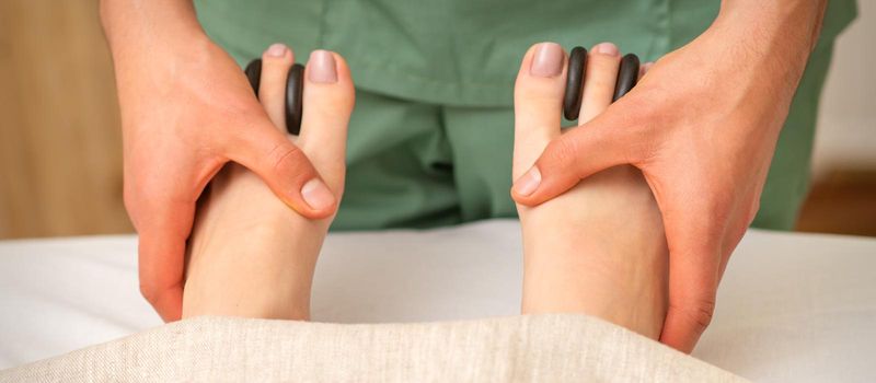 Massager doing feet and toes massage with rocks between a female toes