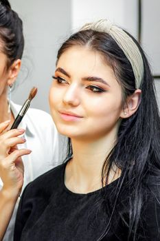 Make-up artist doing makeup for young beautiful bride applying wedding makeup in a beauty salon