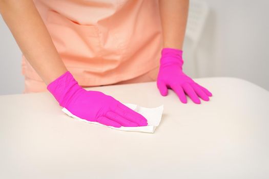 Close up of hands in rubber protective pink gloves cleaning the white surface with a white rag