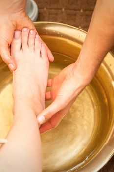 Washing female foot in a special container by male masseur in spa salon