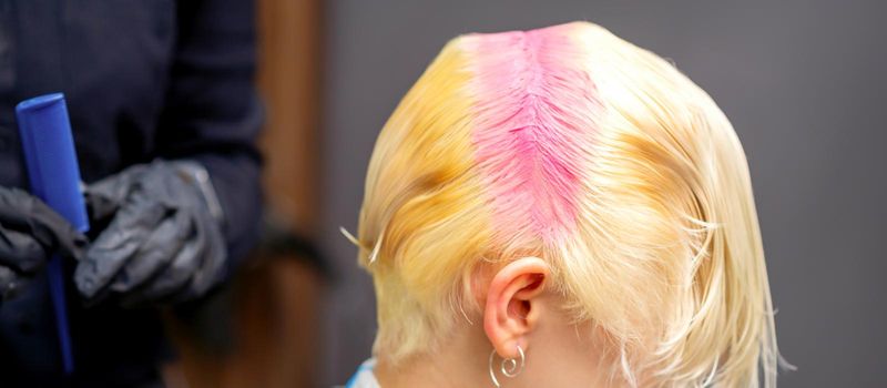 Young caucasian woman tints hair roots in pink color in a beauty salon