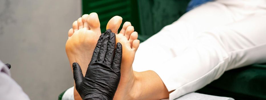 Moisturizing the feet. Hands of pedicure master in black gloves care about female feet. Foot massage. Pedicure beauty salon concept