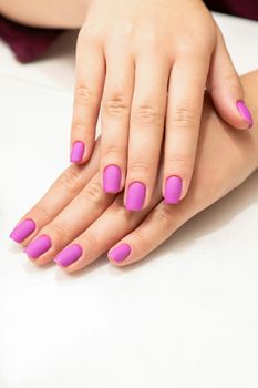 Beautiful fingers with purple nails after nail polish procedure in manicure salon