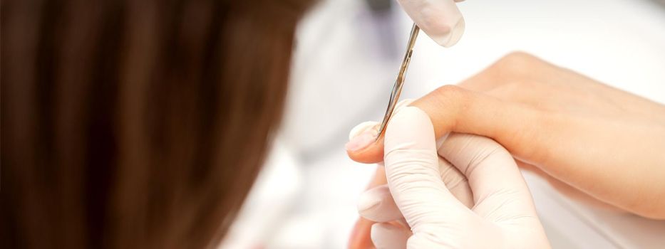 Close up of manicure master with manicure scissors removes cuticles on female nails at a beauty salon