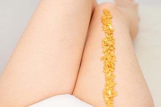 Sugaring concept. Wax granules lying in a row on female legs close up