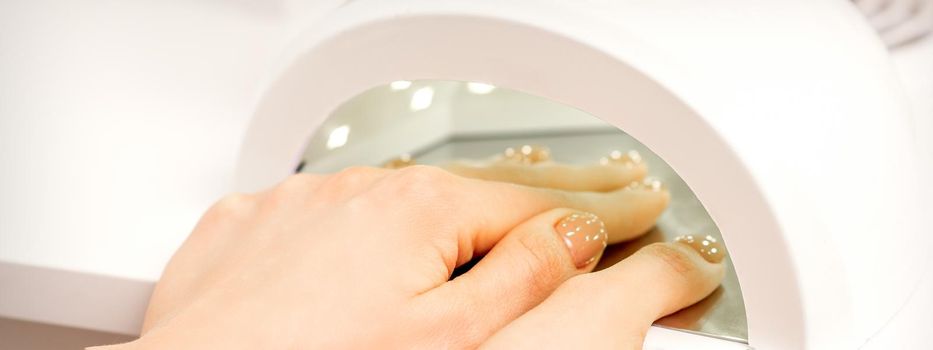 Female hand with manicured fingers dry inside UV light machine in manicure salon