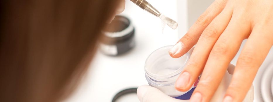 Manicure master applying acrylic powder on the female nails in a beauty salon. Strengthening of nails acrylic powder