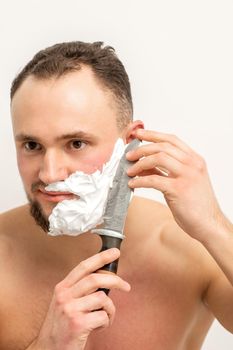 Young caucasian man shaving beard with a big knife on white background