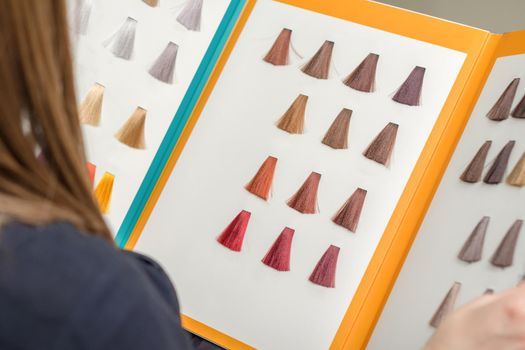 Young brunette woman choosing hair color from palette samples at the beauty salon, hair dyeing concept