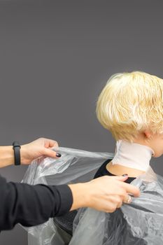 Hairstylist covers neck with cape for a female client in a beauty salon