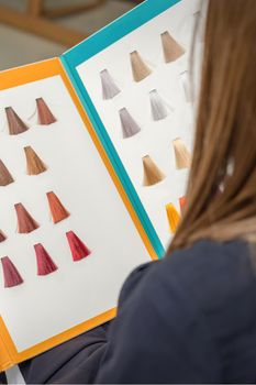 Young brunette woman choosing hair color from palette samples at the beauty salon, hair dyeing concept