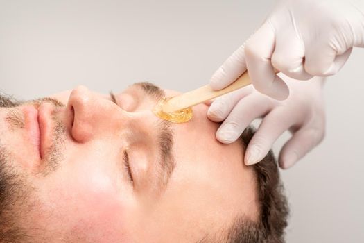 Beautician applying wax paste between eyebrows during the procedure of waxing in the beauty salon