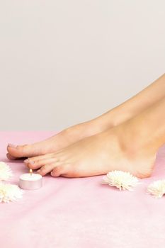 Beautiful white smooth feet of young woman with candles and flowers on pink couch