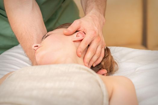 Osteopath doing massage on the female head in rehabilitation clinic center