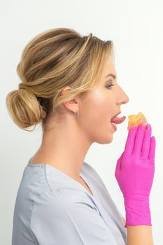 Young beautician licks liquid wax for depilation holding in gloved hands standing on white background. Cosmetologist tastes the sugar paste to taste