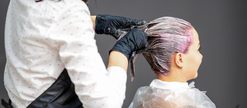 A hairdresser is applying color to the hair of a customer. Hair coloring in a beauty salon. Beauty and people concept. Close-up back view