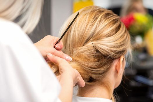 Close-up hairdresser styling blonde hair on the back of the head in a beauty salon