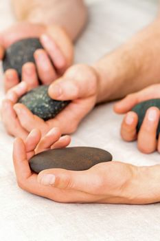 Four hands of male masseurs holding spa stones on white towel top view. Stone massage concept