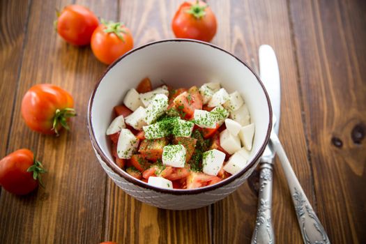 salad of fresh ripe tomatoes with mozzarella and spices in a bowl on a wooden table