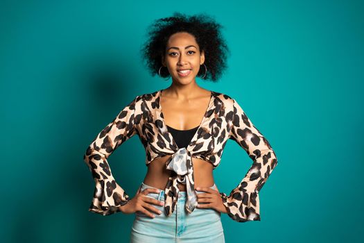 Pretty african woman with afro hair in leopard top smiling to camera over blue wall background. Cute mixed race girl's portrait. High quality photo