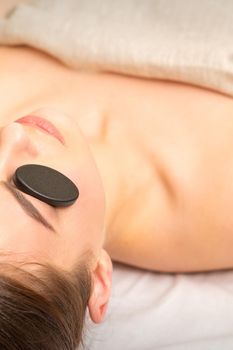 Massage with stones on the eyes of young woman getting a treatment in a beauty spa