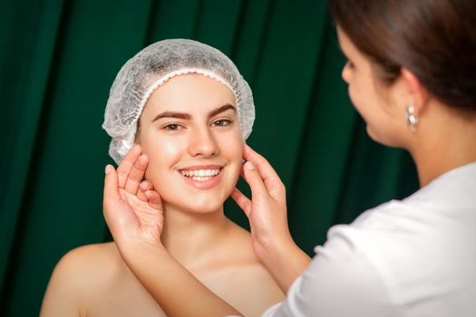 Doctor examining the beautiful face of young smiling woman in beauty clinic