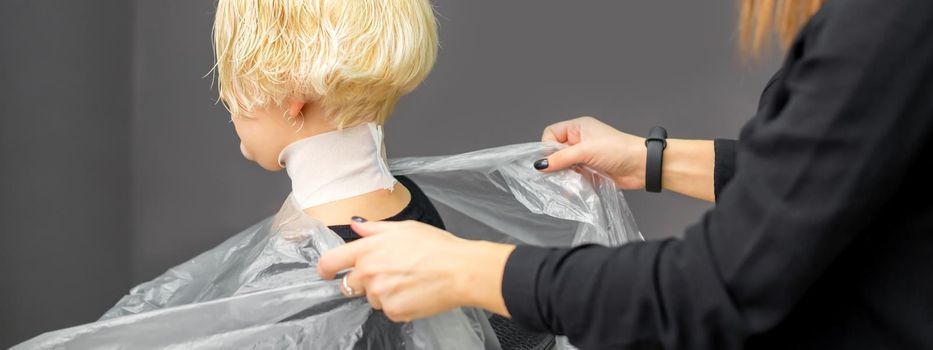 Hairstylist covers neck with cape for a female client in a beauty salon