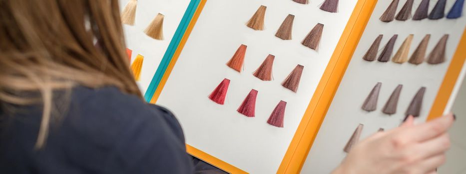 Young brunette woman choosing hair color from palette samples at the beauty salon, hair dyeing concept