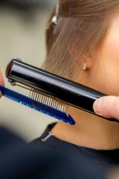 A hairdresser is straightening the hair of the young brunette woman in a beauty salon