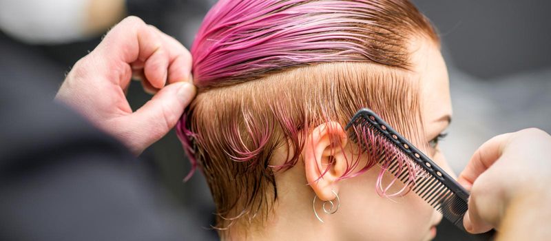 Combing the hair of a young woman during coloring hair in pink color at a hair salon close up